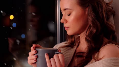 Mujer-Con-Taza-De-Café-O-Té-En-El-Alféizar-De-La-Ventana-En-Casa.-Invierno,-Comodidad-Y-Concepto-De-Personas:-Mujer-Joven-Triste-Con-Jersey-Sentada-En-El-Alféizar-De-La-Ventana-Con-Una-Taza-De-Café-O-Té-En-Casa-Sobre-La-Nieve