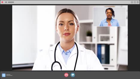 Female-Doctor-in-Islamic-Headscarf-Having-Video-Call-with-Patient-on-Internet.Medium-shot-from-behind-window-blinds-of-Muslim-female-clinician-in-hijab,-uniform-sitting-in-front-of-laptop-at-desk-in-clinic,-consulting-sick-patient-on-video-call-over-internet,-smiling-politely