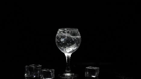 Add-ice-cube-to-shot-of-vodka-in-glass-against-black-background.-Alcohol-drink