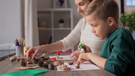 Madre-E-Hijo-Haciendo-Dibujos-De-Hojas-De-Otoño.-Concepto-De-Familia,-Creatividad-Y-Manualidades:-Madre-E-Hijo-Pequeño-Con-Barras-De-Pegamento-Y-Papel-Haciendo-Dibujos-De-Hojas-Secas-De-Otoño,-Piñas-Y-Castañas-En-Casa