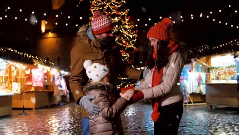 Familia-Feliz-Con-Regalo-En-El-Mercado-Navideño-De-La-Ciudad.-Concepto-De-Celebración-Y-Vacaciones-De-Invierno:-Familia-Feliz-Con-Regalo-En-El-Mercado-Navideño-En-La-Plaza-Del-Ayuntamiento-De-Tallin,-Estonia