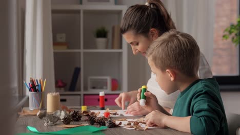 Madre-E-Hijo-Haciendo-Dibujos-De-Hojas-De-Otoño.-Concepto-De-Familia,-Creatividad-Y-Manualidades:-Madre-E-Hijo-Pequeño-Con-Barras-De-Pegamento-Y-Papel-Haciendo-Dibujos-De-Hojas-Secas-De-Otoño,-Piñas-Y-Castañas-En-Casa