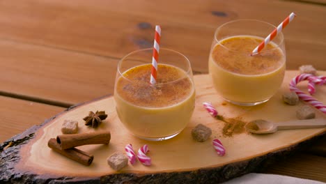 Glasses-of-Eggnog,-Ingredients-and-Spices-on-Wood.christmas,-winter-holidays-and-seasonal-drinks-concept-–-glasses-with-eggnog,-ingredients-and-aromatic-spices-on-wooden-board-over-snow-falling