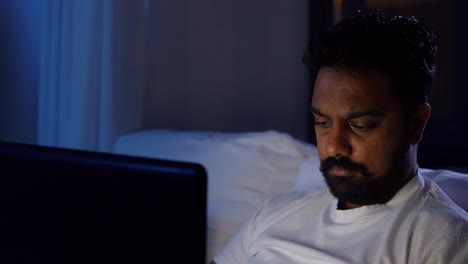 Indian-Man-with-Laptop-in-Bed-at-Home.people,-bedtime-and-rest-concept-–-indian-man-with-chroma-key-green-screen-on-laptop-computer-lying-in-bed-at-home