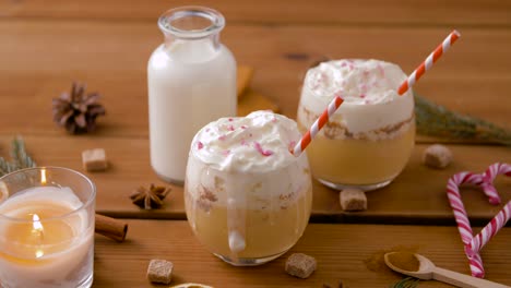 Glasses-of-Eggnog,-Ingredients-and-Spices-on-Wood.christmas,-winter-holidays-and-seasonal-drinks-concept-–-glasses-with-eggnog,-ingredients-and-aromatic-spices-on-wooden-board-over-snow-falling