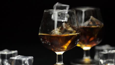 Ice-cubes-dropped-into-glass-of-alcohol-drink-whiskey,-cognac.-Slow-motion