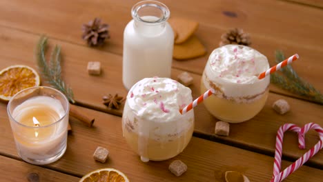 Glasses-of-Eggnog,-Ingredients-and-Spices-on-Wood.christmas,-winter-holidays-and-seasonal-drinks-concept-–-glasses-with-eggnog,-ingredients-and-aromatic-spices-on-wooden-board-over-snow-falling