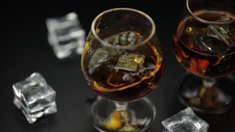 Ice-cube-dropped-into-glass-of-alcohol-drink-whiskey,-cognac.-Slow-motion