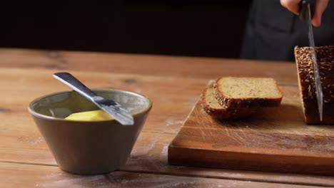 Female-Baker-Cutting-Homemade-Bread-at-Bakery.food-cooking,-baking-and-people-concept-–-female-baker-with-knife-cutting-loaf-of-bread-to-slices-at-bakery-or-kitchen