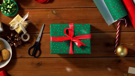 Woman-Packing-Christmas-Gifts-at-Home-Over-Snow.holidays,-new-year-and-christmas-concept-–-woman-holding-gift-box-in-green-wrapping-paper-package-with-red-bow-and-name-tag-at-home-over-snow