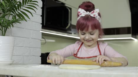 Cooking-pizza.-Little-child-in-apron-roll-dough-with-rolling-pin-at-home-kitchen