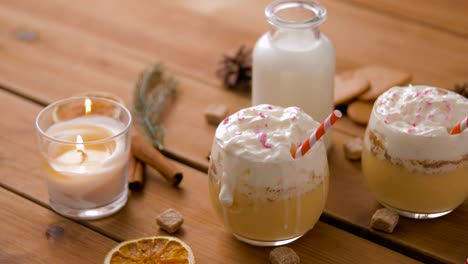 Glasses-of-Eggnog,-Ingredients-and-Spices-on-Wood.christmas,-winter-holidays-and-seasonal-drinks-concept-–-glasses-with-eggnog,-ingredients-and-aromatic-spices-on-wooden-board-over-snow-falling