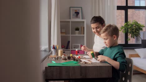 Madre-E-Hijo-Haciendo-Dibujos-De-Hojas-De-Otoño.-Concepto-De-Familia,-Creatividad-Y-Manualidades:-Madre-E-Hijo-Pequeño-Con-Barras-De-Pegamento-Y-Papel-Haciendo-Dibujos-De-Hojas-Secas-De-Otoño,-Piñas-Y-Castañas-En-Casa