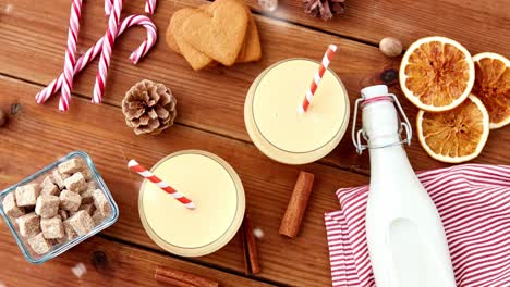 Glasses-of-Eggnog,-Ingredients-and-Spices-on-Wood.christmas,-winter-holidays-and-seasonal-drinks-concept-–-glasses-with-eggnog,-ingredients-and-aromatic-spices-on-wooden-board-over-snow-falling