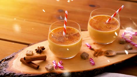 Glasses-of-Eggnog,-Ingredients-and-Spices-on-Wood.christmas,-winter-holidays-and-seasonal-drinks-concept-–-glasses-with-eggnog,-ingredients-and-aromatic-spices-on-wooden-board-over-snow-falling