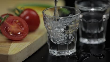 Gießen-Sie-Alkoholgetränk-Wodka-Aus-Einer-Flasche-In-Ein-Schnapsglas.-Oberfläche-Mit-Snacks