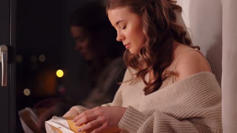 Woman-Opening-Ribbon-on-Wrapped-Christmas-Gift-at-Home.Midsection-of-woman-sitting-with-cross-legs-opening-ribbon-on-wrapped-Christmas-gift-at-home