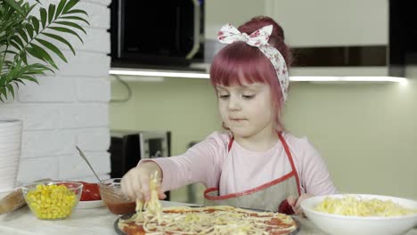 Cooking-pizza.-Little-child-in-apron-adding-grated-cheese-to-dough-in-kitchen