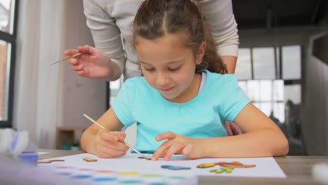 Little-Daughter-with-Mother-Painting-Wooden-Blanks.family,-motherhood-and-leisure-concept-–-mother-spending-time-with-her-little-daughter-painting-wooden-craftwork-with-brush-and-colors-at-home