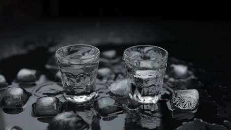 Add-ice-cubes-to-shot-of-vodka-in-glass-against-black-background.-Alcohol-drink