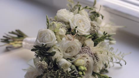 Wedding-golden-rings-lie-on-beautiful-wedding-white-rose-flowers-bouquet-on-white-window-sill