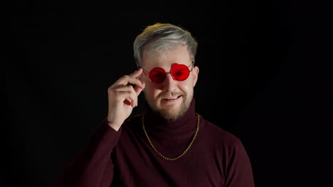 Handsome-man-in-stylish-blouse-taking-off-red-sunglasses,-facial-expression-on-black-background