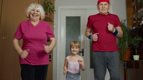 Granddaughter-and-mature-grandparents-in-sportswear-making-sports-jogging-workout-exercises-at-home