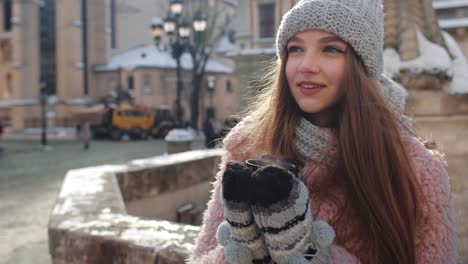 Stylish-woman-tourist-with-hot-drink-in-cup-looking-around-through-city-street-during-vacations