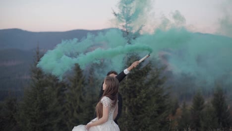 Newlyweds.-Caucasian-groom-with-bride-on-mountain-slope-with-smoke-bomb