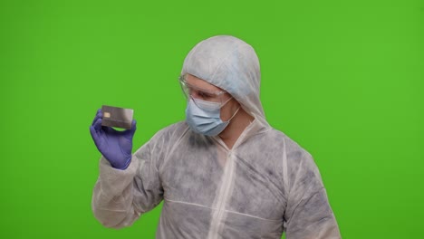 Doctor-in-PPE-suit-with-coronavirus-vaccine-ampoule-and-credit-card-in-hands-on-green-chroma-key