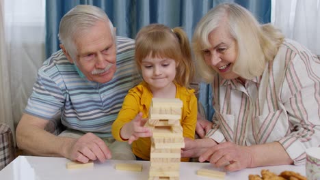 Aufgeregtes-Kind,-Mädchen,-Das-Mit-Der-älteren-Großmutter-Und-Dem-Großvater-An-Einem-Brettspiel-Mit-Bauklötzen-Beteiligt-Ist