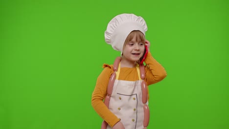 Child-girl-cook-chef-receiving-online-order,-talking-on-mobile-phone-making-conversation-with-client