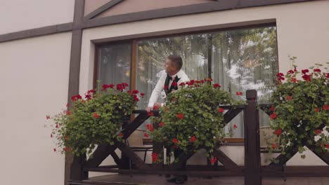 Handsome-groom-man-wearing-white-jacket-stand-on-balcony-at-home-gets-ready-before-date-or-meeting