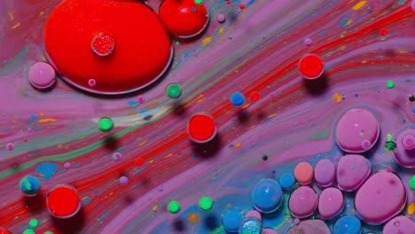 Top-view-movement-of-red-oil-ink-drops-bubbles,-multicolored-artistic-paint-surface-background