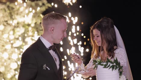 Newlyweds-eating-wedding-cake,-lovely-bride-and-groom-couple-cutting-dessert-with-a-knife-outdoors