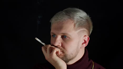 Stylish-addicted-young-man-with-blue-eyes-in-trendy-clothes-looking-at-camera,-smoking-cigarette