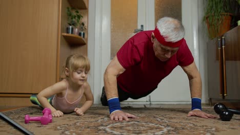 Child-kid-girl-with-senior-grandfather-in-sportswear-making-sports-workout-push-up-exercises-at-home