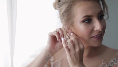 Beautiful-and-lovely-bride-in-wedding-dress-and-veil-puts-on-earrings