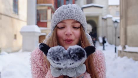 Young-woman-traveler-tourist-showing-snow-in-hands-palms-to-camera-and-blowing-it-on-city-street