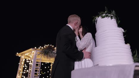 Newlyweds-making-a-kiss-after-cut-of-wedding-cake,-bride-groom-behind-of-wedding-three-tiered-cake