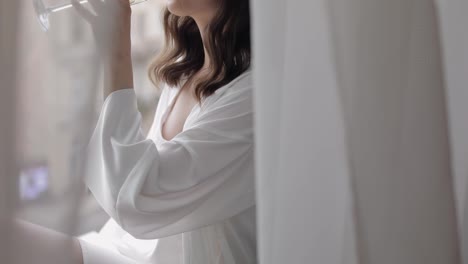 Bride-in-boudoir-dress-sitting-on-window-sill-wedding-morning-preparations-woman-in-night-gown,-veil