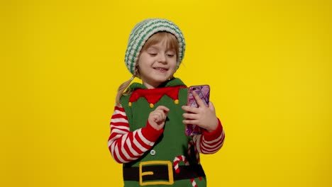 Kid-child-girl-in-Christmas-elf-Santa-Claus-helper-costume-making-a-video-call-on-mobile-phone