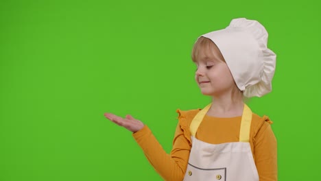 Child-girl-dressed-like-chef-cook-pointing-at-left-on-blank-space,-place-for-your-advertisement-logo