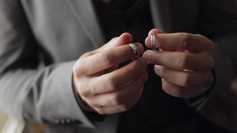 Groom-in-gray-jacket-holding-wedding-rings-on-palm-of-his-hand,-man-touches-the-rings,-slow-motion