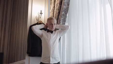 Groom-man-adjusts-bow-tie,-preparing-to-go-to-the-bride,-businessman-in-white-shirt,-wedding-day