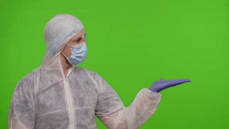 Medical-doctor-in-protective-PPE-suit-pointing-at-right-on-blank-space-on-chroma-key-background