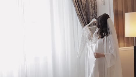 Bride-in-lingerie-dancing-with-her-wedding-dress-at-home-near-window,-white-boudoir-dress-and-veil