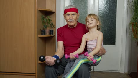 Child-kid-girl-with-senior-grandfather-in-sportswear-making-sports-workout-exercises-with-dumbbells