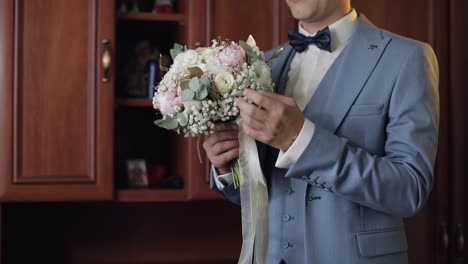 Groom-with-wedding-bouquet-in-his-hands-at-home.-White-shirt,-jacket