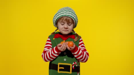 Kid-girl-in-Christmas-elf-Santa-helper-costume-holding-mandarin-fruits.-New-Year-holiday-celebration